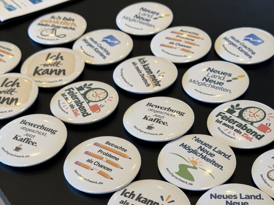 BerufSprachWerk-Buttons mit Mut-Sprüchen auf dem Tisch